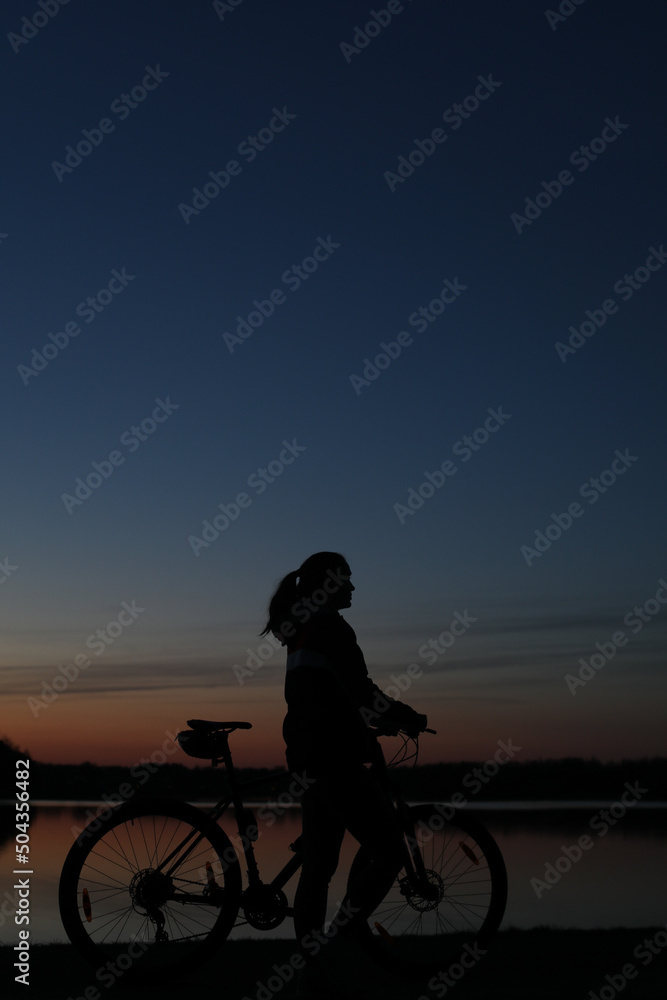 Obraz premium Silhouette of woman with mountain bike on colorful blue sky sunset background. Active outdoors lifestyle