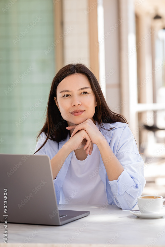 smiling and dreamy woman looking away near laptop on cafe terrace. smiling and dreamy woman looking away near laptop on cafe terrace.