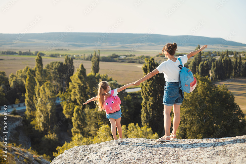 Happy mother and little daughter standing on top of the mountain, feeling free and enjoy the views on summer vacation