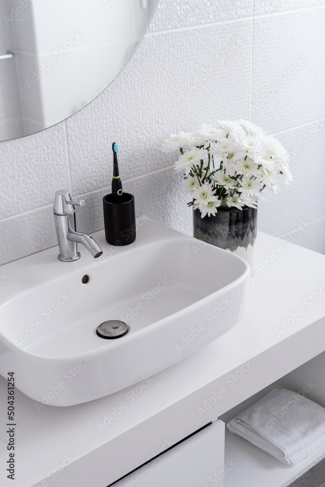 Fototapeta premium Electric toothbrush, flowers and white sink in bathroom
