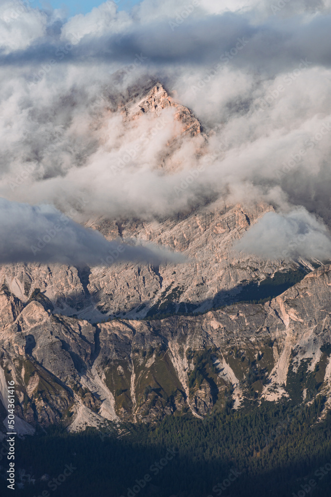 The peaks of the Dolomites, with the lights of the sunset, immersed in the fog, near the town of Cortina d'Ampezzo, Italy - October 2021.