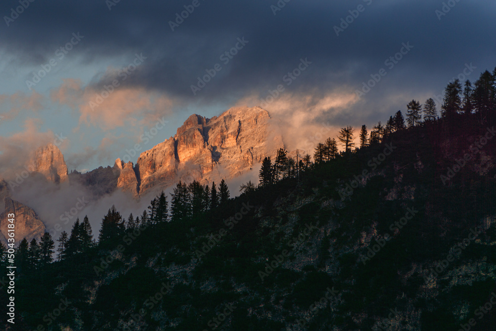The peaks of the Dolomites, with the lights of the sunset, immersed in the fog, near the town of Cortina d'Ampezzo, Italy - October 2021.