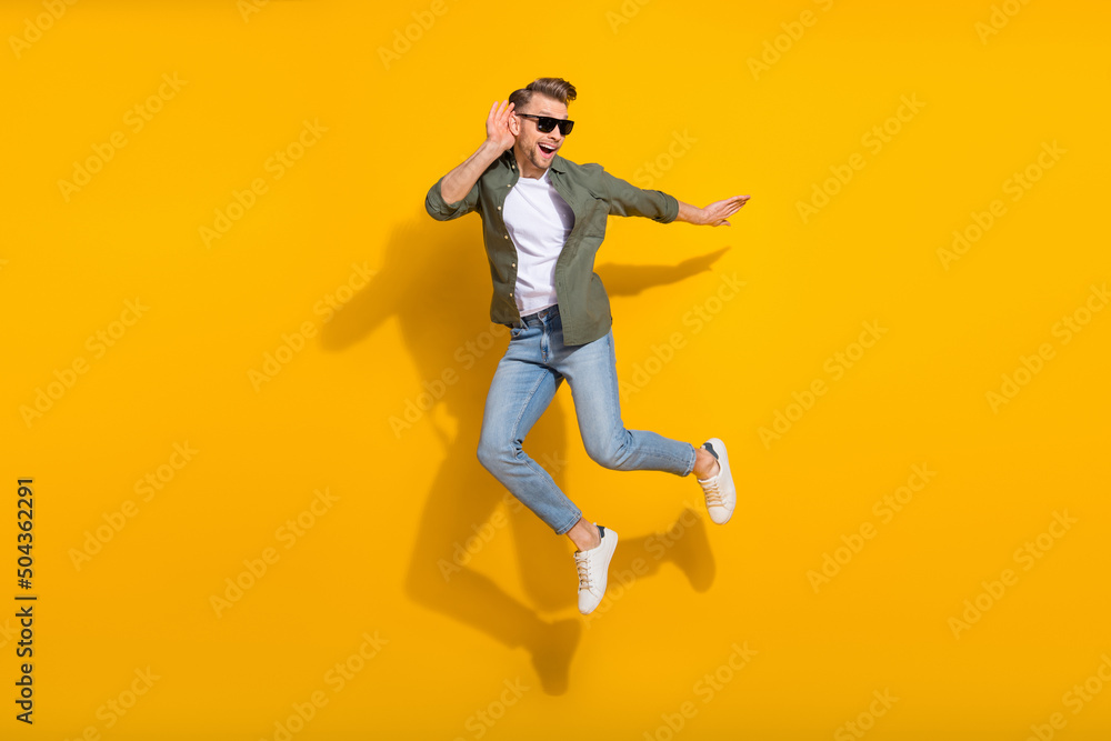 Full length body size view of attractive cheerful curious guy jumping listening isolated over bright yellow color background