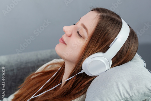 Relaxing time on sofa. Beautiful young girl lay down on sofa and listening to the music with headphone