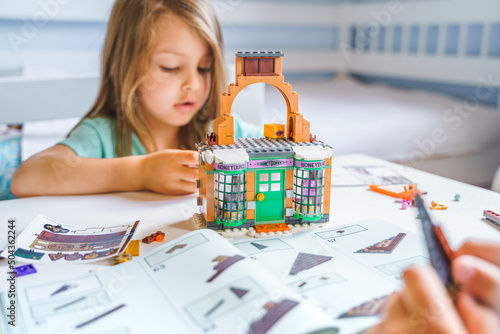 Girls, sisters play kids constructor, build house from bricks, blocks by assembly instrustions. Children activity at home in playroom. Intelligent development of fine motor skills photo