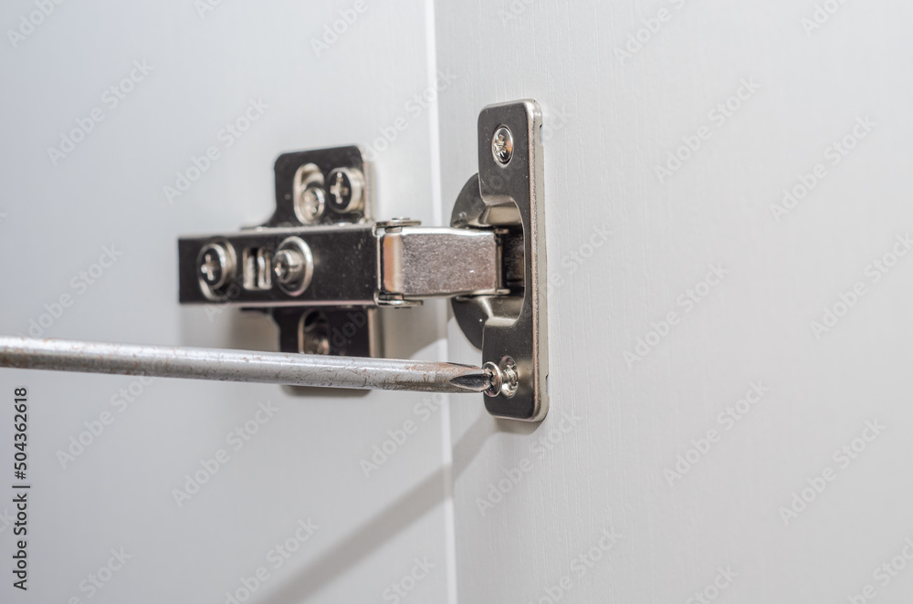 The furniture maker installs furniture hinges in the closet, tightening the screw with a screwdriver The furniture maker installs furniture hinges in the closet, tightening the screw with a screwdriver