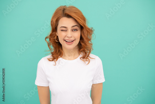 winking redhead woman with curly hair on blue background