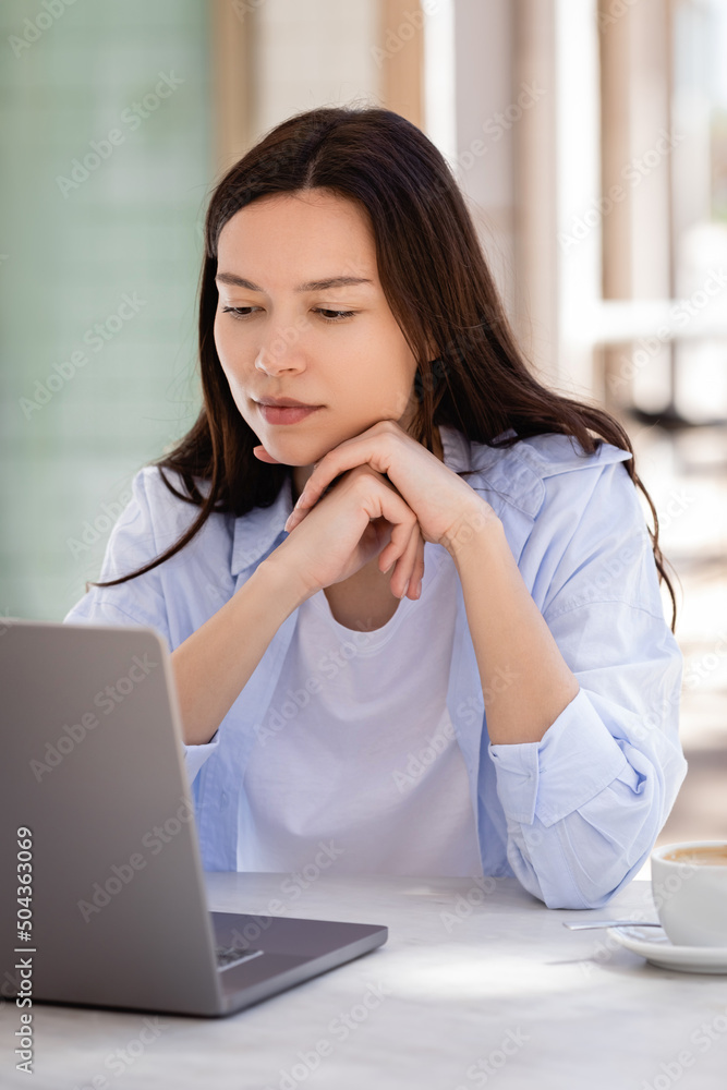 brunette woman sitting on cafe terrace and looking at laptop. brunette woman sitting on cafe terrace and looking at laptop.