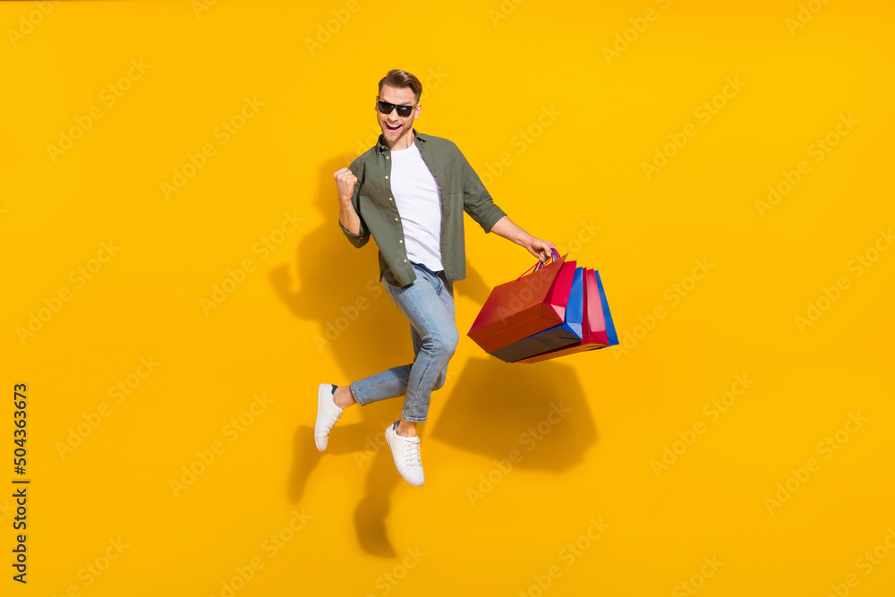 Full length body size view of attractive cheerful guy jumping buying gifts things rejoicing isolated over bright yellow color background