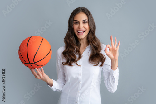 Happy woman with ok sign hold basketball ball, isolated on gray background. © Olena