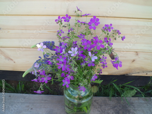 purple flowers in a glass jar on a wooden wall background
