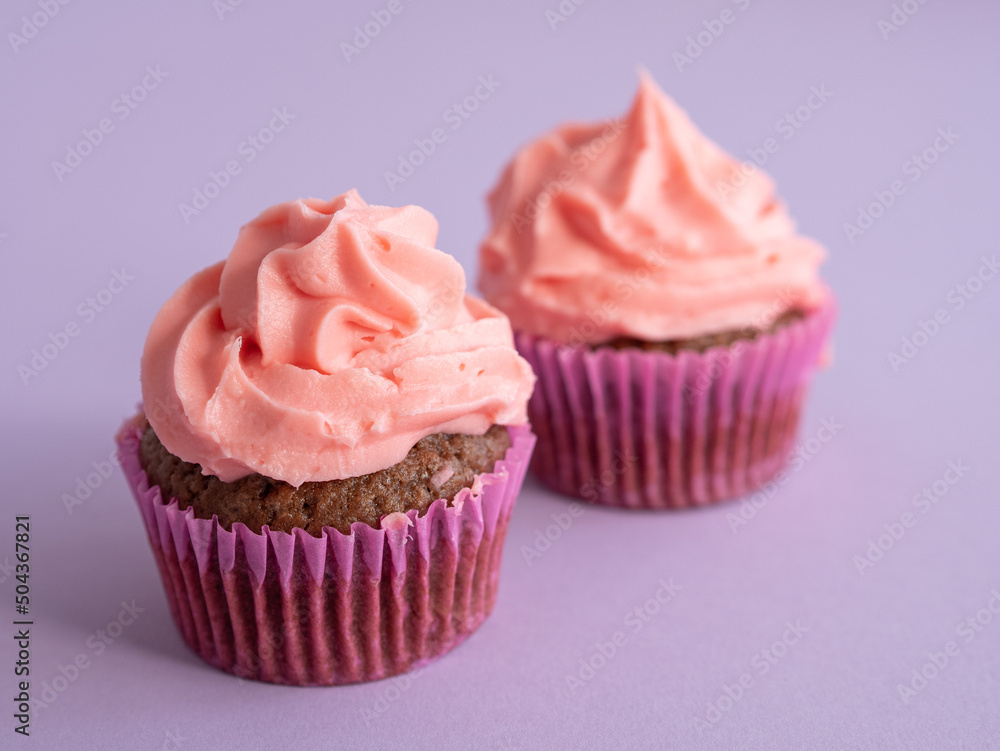 Two cupcakes on a purple background with a cap of pink cream