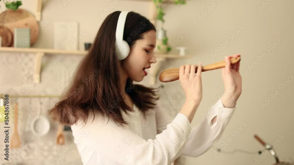 Portrait of attractive cheerful woman singing song in spoon on dometic kitchen in slow motion. Young woman dancing and have fun on the kitchen. Portrait of attractive cheerful woman singing song in spoon on dometic kitchen in slow motion. Young woman dancing and have fun on the kitchen.