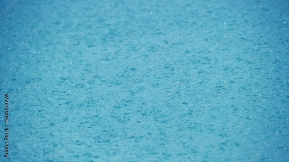 Rain Water Droplets Splash into a Blue Puddle. Slow motion close up of rain hitting a puddle during a storm in rainy season Rain Water Droplets Splash into a Blue Puddle. Slow motion close up of rain hitting a puddle during a storm in rainy season