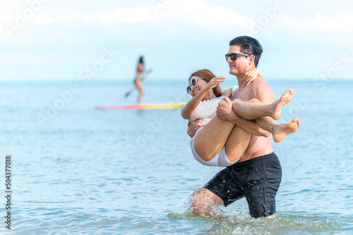 young man holding girlfriend and wading in ocean at the beach - sweet and funny lover couple