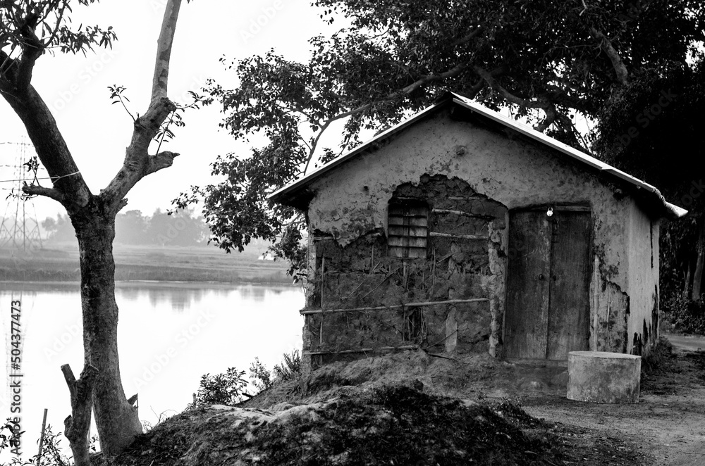 A dilapidated and abandoned hut by the river outside a village