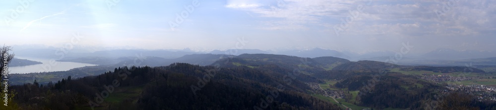 Wide angle panoramic view from local mountain Uetliberg with Lake Zürich and Swiss Alps in the background on a blue cloudy spring day. Photo taken April 14th, 2022, Zurich, Switzerland.