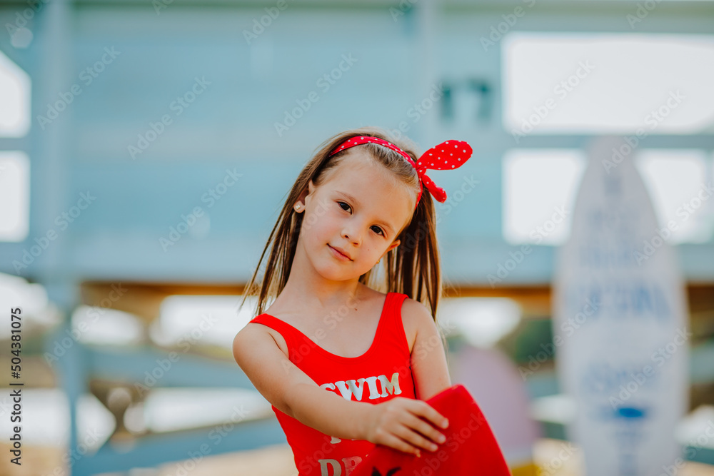 Pretty little girl in red bikini posing with small surfboard like a
