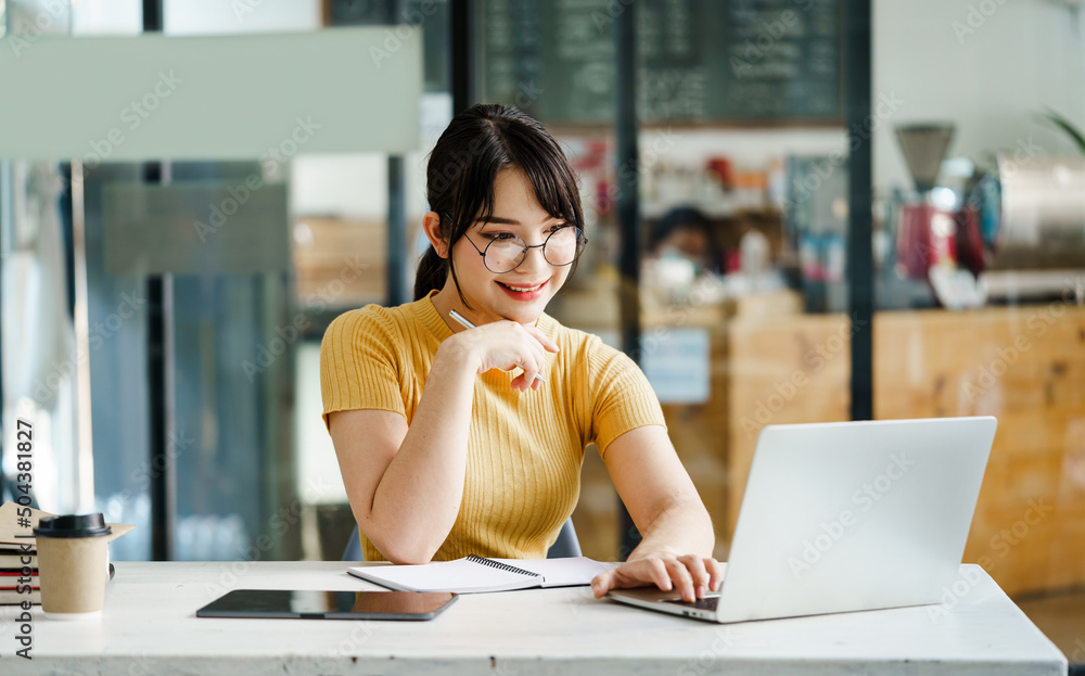 An asian woman sitting at meeting table and looking at laptop with smile. Employee waiting for meeting hour. An asian woman sitting at meeting table and looking at laptop with smile. Employee waiting for meeting hour.