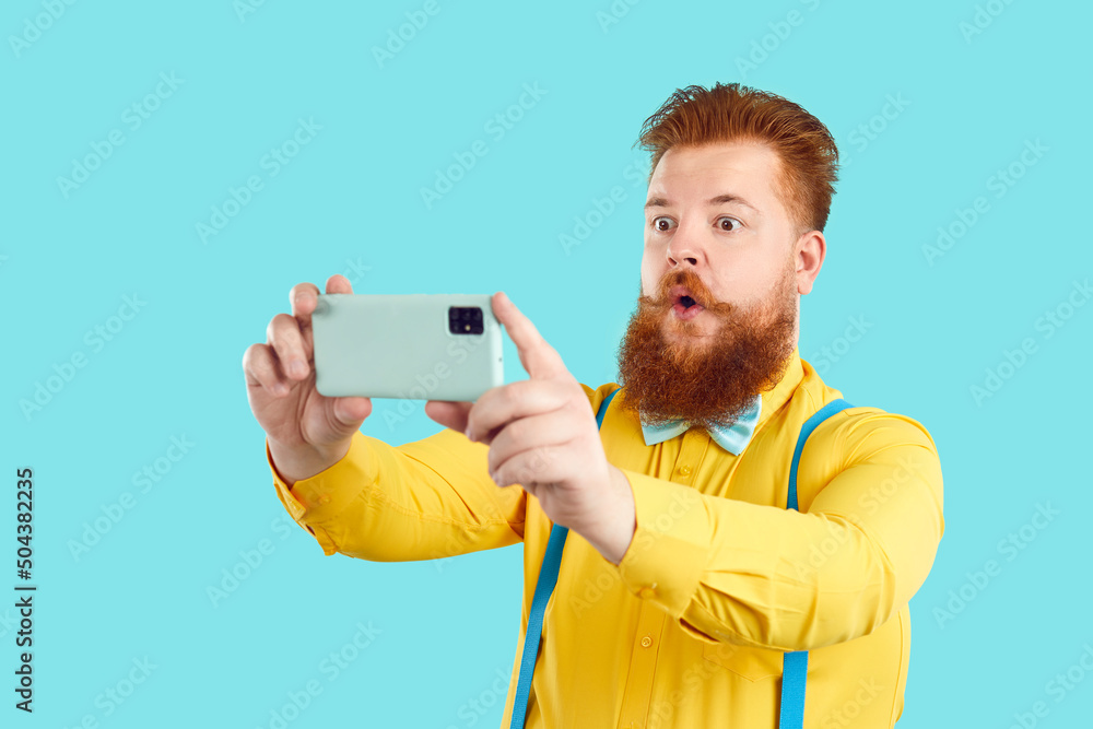 Funny fat man in funky outfit takes selfie on his modern mobile phone. Plus  size bearded