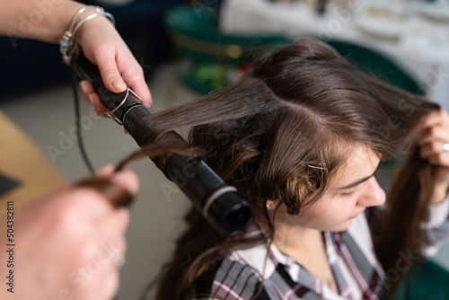 The stylist curls the girl's hair with a curling iron