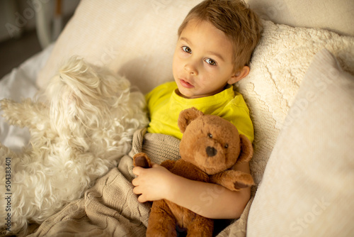 Cute little preschool boy with his pet dog, playing together in bed