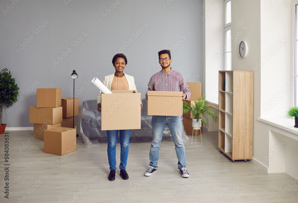 Portrait of happy multiethnic family buyers with boxes excited to move into new apartment together. Smiling multiracial couple renters relocate to own house or home. Real estate, rent concept. Portrait of happy multiethnic family buyers with boxes excited to move into new apartment together. Smiling multiracial couple renters relocate to own house or home. Real estate, rent concept.