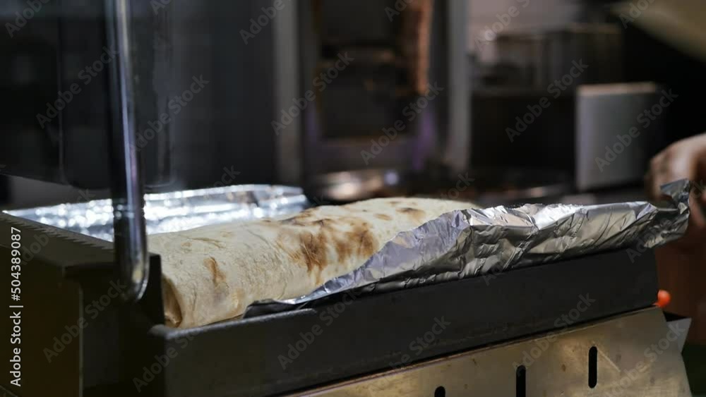a cook in a black glove took out a cooked doner kebab wrapped in thin pita bread from the grill. Shawarma is cooked and ready to eat. Fast food concept a cook in a black glove took out a cooked doner kebab wrapped in thin pita bread from the grill. Shawarma is cooked and ready to eat. Fast food concept