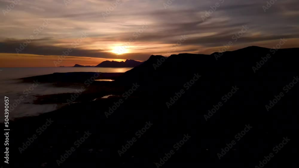 Mountain silhouettes as sunset illuminates sky in warm tones over ocean; aerial Mountain silhouettes as sunset illuminates sky in warm tones over ocean; aerial