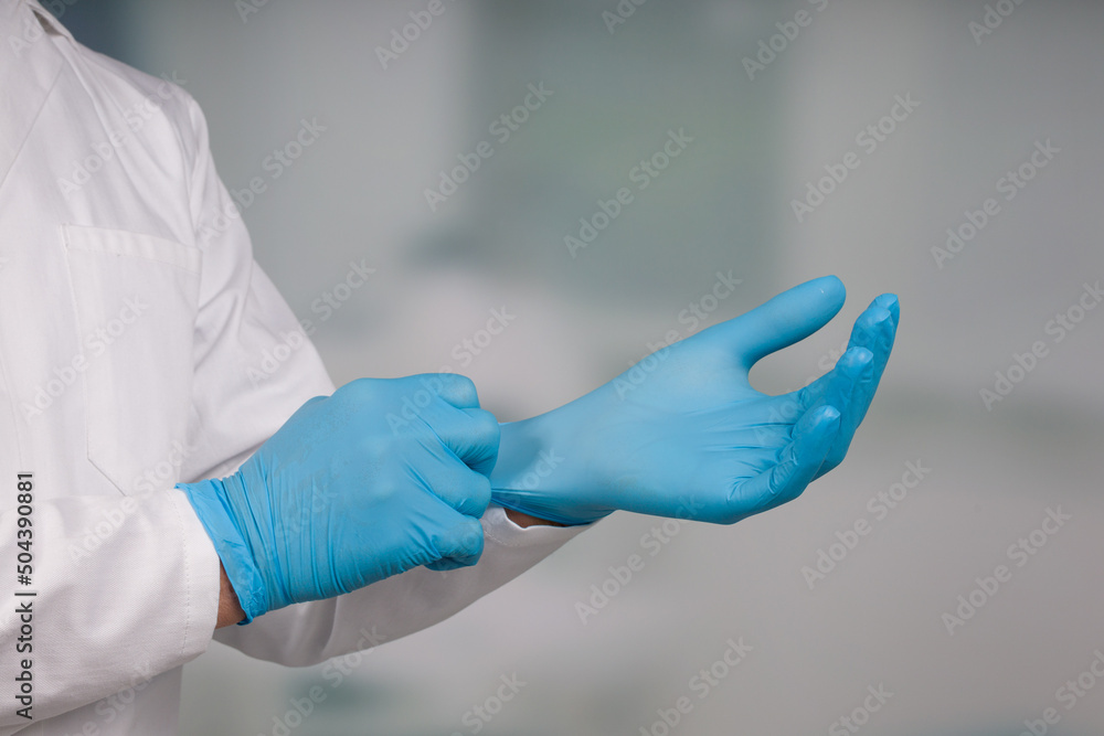 Close-up of hands putting on medical gloves in front of a clinic/ICU room Close-up of hands putting on medical gloves in front of a clinic/ICU room