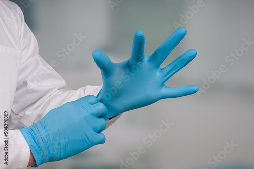 Close-up of hands putting on medical gloves in front of a clinic/ICU room 