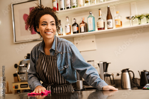 Black barista woman wearing apron smiling while working in cafe