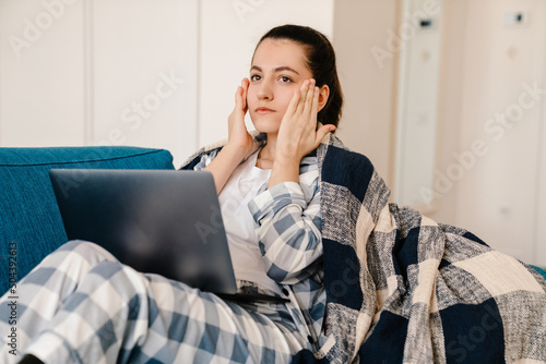 Young woman wearing pajama using laptop while resting on couch