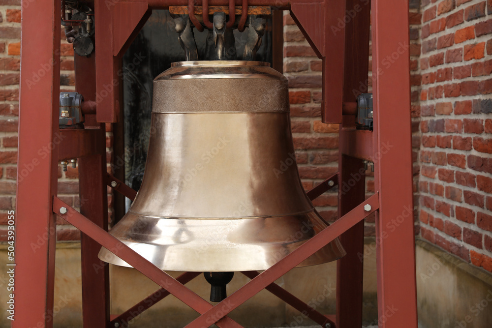 Wooden construction with large old bronze bell near brick wall outdoors
