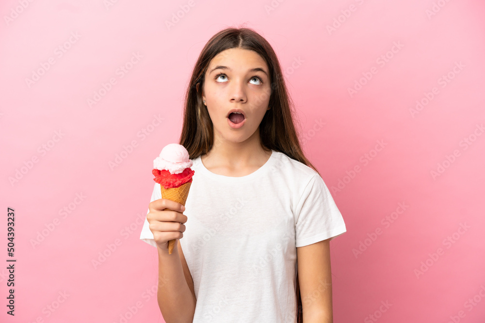 Little girl with a cornet ice cream over isolated pink background looking up and with surprised expression Little girl with a cornet ice cream over isolated pink background looking up and with surprised expression