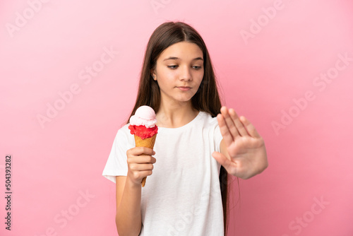 Little girl with a cornet ice cream over isolated pink background making stop gesture and disappointed