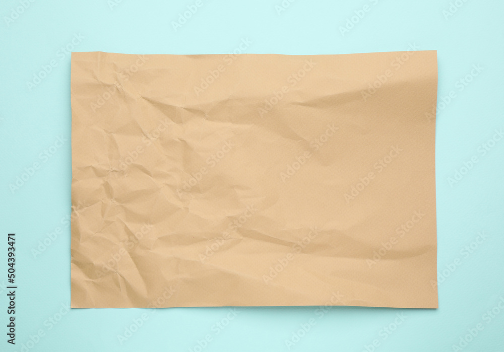Sheet of crumpled brown paper on light blue background, top view Sheet of crumpled brown paper on light blue background, top view