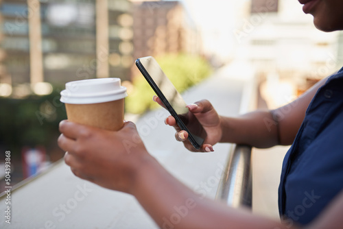 An unidentified Black woman texts during her coffee break outside office