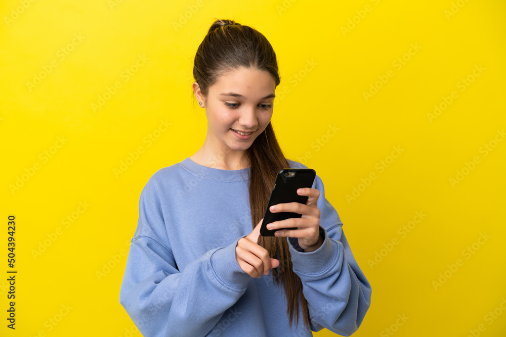 Little girl over isolated yellow background sending a message or email with the mobile