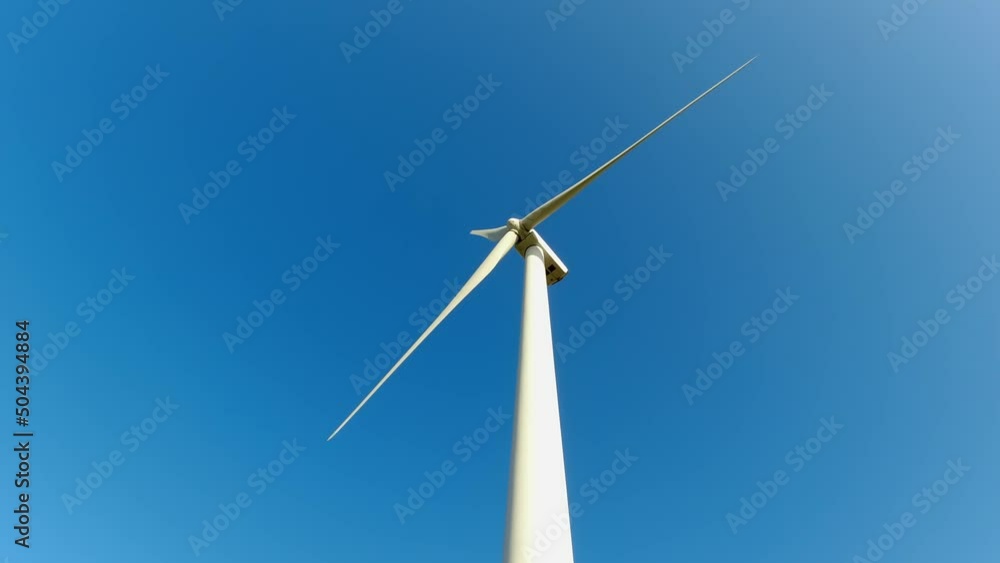 Large wind turbine with blades in the field below view. Blue sky panorama. Windmills farm generating green energy. Sustainable alternative energy. Slow movement. Large wind turbine with blades in the field below view. Blue sky panorama. Windmills farm generating green energy. Sustainable alternative energy. Slow movement.