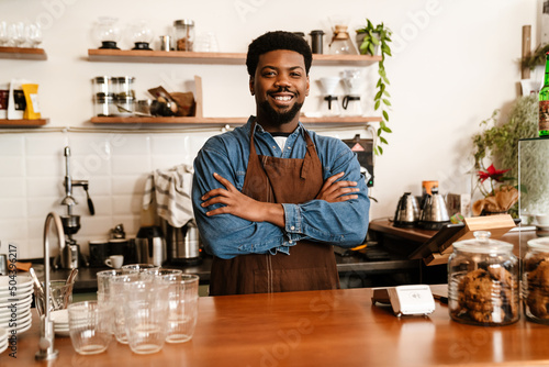 Black bearded man wearing apron smiling while working in cafe