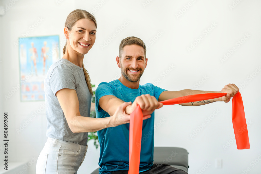 Fototapeta premium Modern rehabilitation physiotherapy woman worker with man client using red elastic
