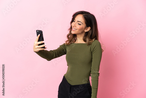 Young caucasian woman isolated on pink background making a selfie