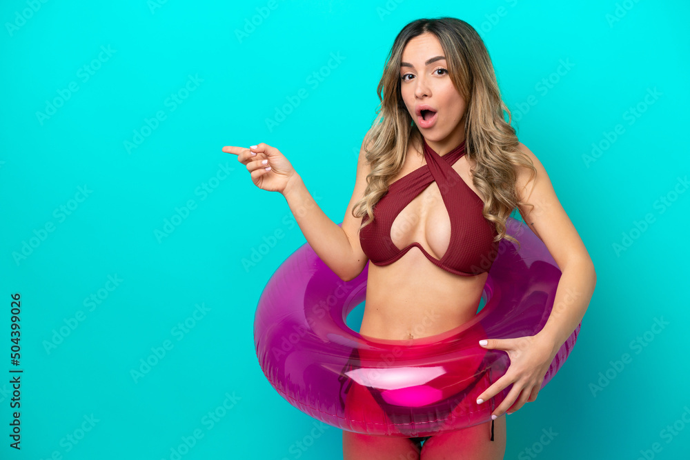 Woman in swimsuit holding floater isolated on blue background surprised and pointing finger to the side Woman in swimsuit holding floater isolated on blue background surprised and pointing finger to the side