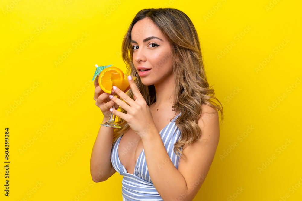 Young caucasian woman isolated on yellow background in swimsuit and holding a cocktail Young caucasian woman isolated on yellow background in swimsuit and holding a cocktail
