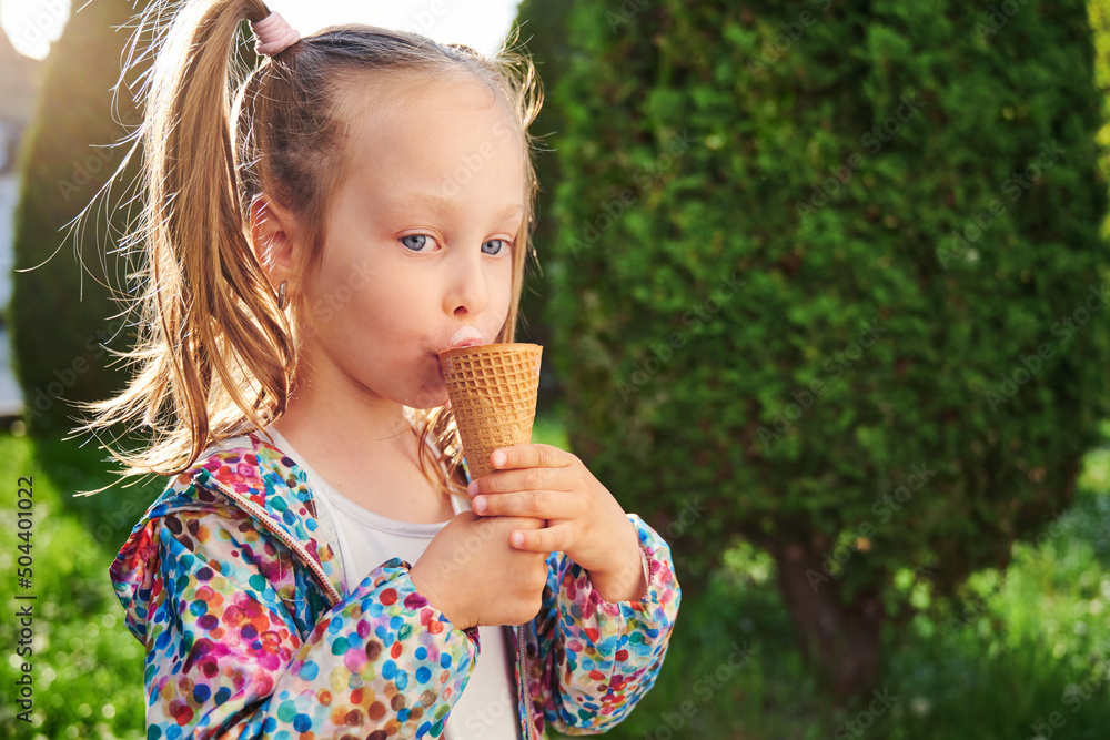Cheerful kid girl with ice cream in waffle cone is eating licking tongue ice cream. Close-up ice cream. Summer dessert for kid and summer time concept Cheerful kid girl with ice cream in waffle cone is eating licking tongue ice cream. Close-up ice cream. Summer dessert for kid and summer time concept