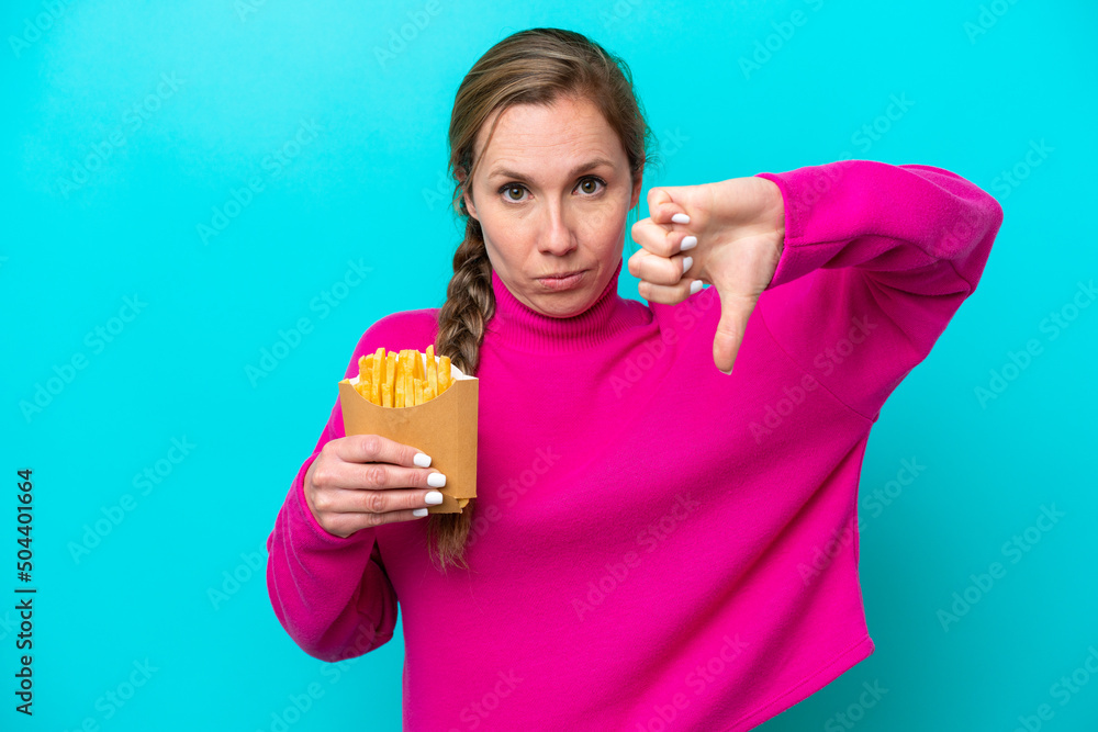 Young caucasian woman holding fried chips isolated on blue background showing thumb down with negative expression Young caucasian woman holding fried chips isolated on blue background showing thumb down with negative expression