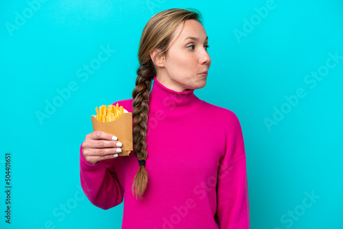 Young caucasian woman holding fried chips isolated on blue background looking to the side