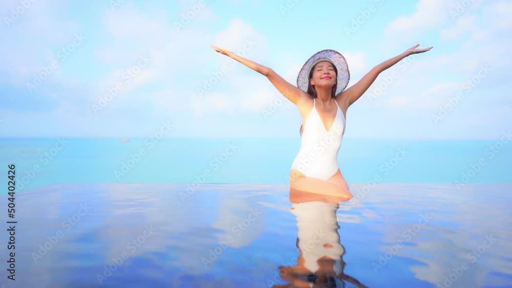 A young attractive woman sitting on the edge of a swimming pool raises her arms in joy. Title space A young attractive woman sitting on the edge of a swimming pool raises her arms in joy. Title space