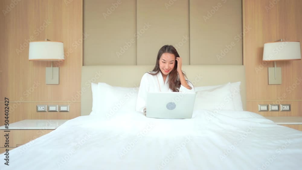 In a work from anywhere world, a young woman in a bathrobe works on her laptop while enjoying a huge comfortable bed. In a work from anywhere world, a young woman in a bathrobe works on her laptop while enjoying a huge comfortable bed.